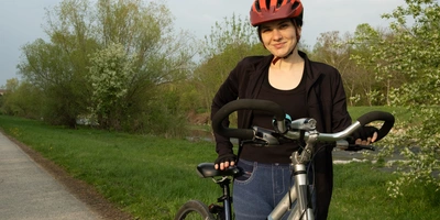 Fahrradsattel speziell für Frauen Testsieger Junge Frau mit Helm lächelt und steht neben ihrem Fahrrad auf einem Radweg.