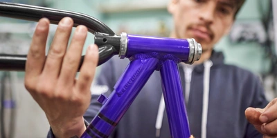 Hände montieren Teile an einem lila Fahrradrahmen in einer Werkstatt.