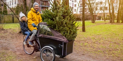 Mann fährt mit Tochter und Weihnachtsbaum auf Lastenrad