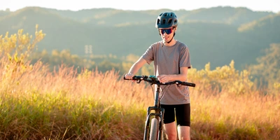 Fahrradfahrer steht mit seinem Fahrrad auf einem Feldweg und klickt auf dem Smartphone