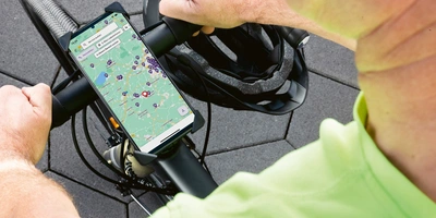 Service Finder in der linexo App Eine Hand mit einem Smartphone auf einem Fahrradlenker, im Hintergrund ein Helm.