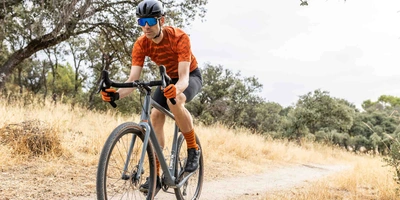 Mann mit Helm fährt auf Gravelbike über einen Weg durch die Natur.