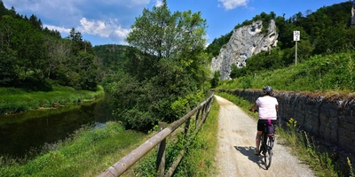 Hohenzollern Radweg: Etappen, Länge & Tipps für die Tour Radfahrer auf einem Weg entlang eines Flusses, umgeben von grüner Natur und Felsen.