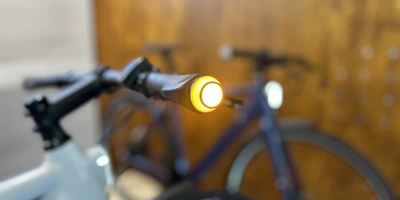 Die Fahrräder und E-Bikes von Ellipse kommen bereits mit integrierter Beleuchtung für Tag und Nacht Nahaufnahme eines Fahrradlenkers mit einem leuchtenden gelben Lenkerlicht