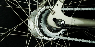 Detailansicht eines Fahrradnaben mit Speichen und Kette auf schwarzem Hintergrund.