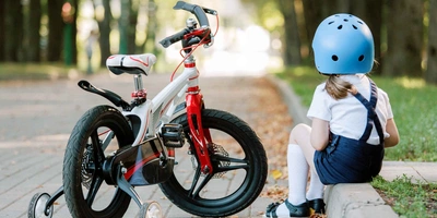 Kind mit Helm sitzt neben Fahrrad auf Bordstein.