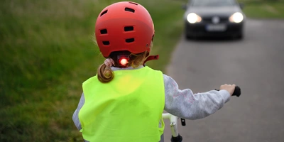 Beleuchtung Kinderfahrrad: Sicher mit dem richtigen Fahrradlicht Ein Kind mit rotem Helm und reflektierender Weste fährt mit dem Fahrrad auf der Straße.