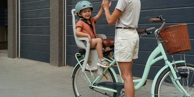 Mutter klatscht mit ihrem Kind ein, dass auf einem Fahrradkindersitz sitzt