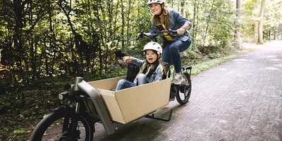 Frau fährt mit Kind und Helm auf Lastenrad durch den Wald