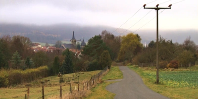 Landschaft mit einer kurvigen Straße, herbstlichen Bäumen und einem Dorf im Hintergrund.