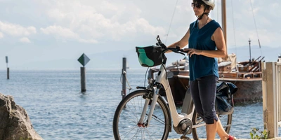 Frau mit Helm steht neben Fahrrad an einem See.