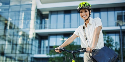 Business Urban Frau Lächelnde Frau in Businesskleidung mit Helm schiebt ihr Fahrrad vor einem Gebäude