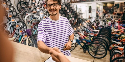 Ein junger Mann in gestreiftem Shirt reicht einem anderen die Hand in einem Fahrradgeschäft.
