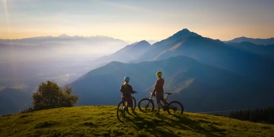 Zwei Fahrradfahrerinnen stehen auf einem Berg und schauen in die Ferne