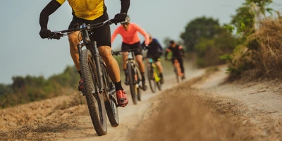 Fahrradmarken Mountainbike: Die wichtigsten MTB Marken Vier Mountainbiker fahren auf einem staubigen Pfad durch eine grüne Landschaft.