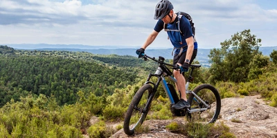 Mann fährt auf E-Mountainbike durch Berge und Wald.