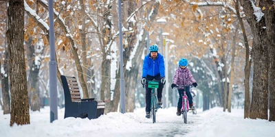 So bist du sicher in der kalten Jahreszeit unterwegs. Mann und Kind fahren Fahrrad im Schnee.