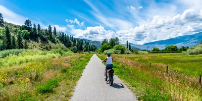 Ein Radfahrer auf einem schmalen Weg, umgeben von grünen Feldern und blauer Himmel.