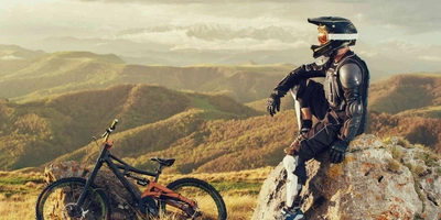 Unentbehrlich für Fahrten durch das Gelände - MTB Protektoren Downhill-Biker sitzt mit Schutzkleidung auf einem Fels