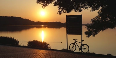 Blick auf einen See bei Sonnenuntergang Silhouette von Bäumen Schild Fahrrad Spielgelung Reflektion der Sonne auf dem See