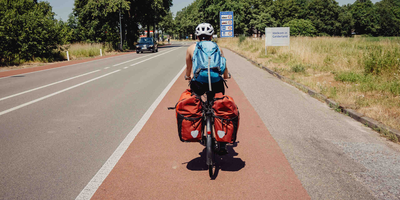 Frau fährt auf Fahrrad mit Gepäcktaschen über den Radweg.