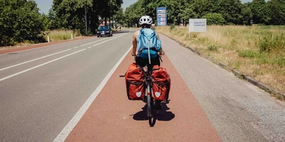 Frau fährt auf Fahrrad mit Gepäcktaschen über den Radweg.