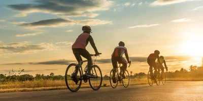 Die Radsaison beginnt - die ersten Sonnenstrahlen lassen sich sehen Vier Fahrradfahrer fahren dem Sonnenaufgang entgegen