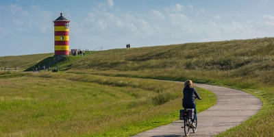 Frau fährt mit einem Fahrrad zum Pilsumer Leuchtturm in Ostfriesland