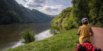 Fahrradfahrerin schaut vom Flussufer auf die Saarschleife
