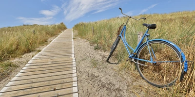 Radwege Langeoog: Touren, Highlights & Geheimtipps Blaues Fahrrad steht an einem Holzsteg, umgeben von Wiesen und Wolken am Himmel.