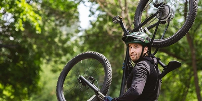 Mann trägt Mountainbike auf Schulter