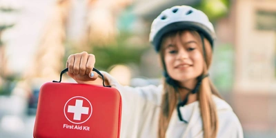 Reiseapotheke für Fahrradfahrende Frau hält eine Reiseapotheke in der Hand und trägt einen Fahrradhelm