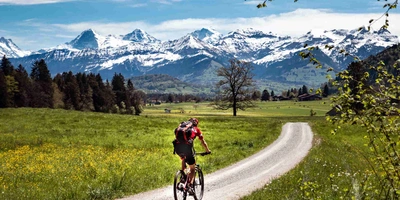 Mann fährt auf Fahrrad durch schöne Landschaft vor Bergkette
