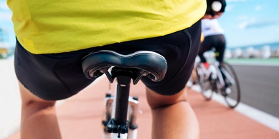 Sitzknochenabstand messen: Ideale Sattelbreite finden mit linexo Fokus auf den Fahrradfahrer mit gelbem Trikot, Blick auf den Sattel und Asphaltweg.