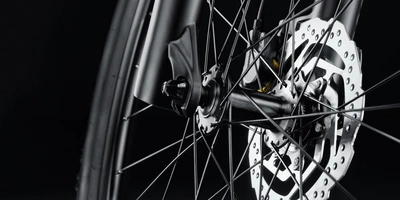 Nahaufnahme eines Fahrradbremsen mit Speichen auf schwarzem Hintergrund.