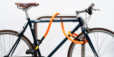 texlock Test – lohnt sich das Textil-Fahrradschloss? Blaues Fahrrad mit einem orangefarbenen Schloss, an einem Metallpfosten gesichert.