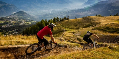 Zwei Mountainbiker fahren die hügelige Strecke in malerischer Berglandschaft.