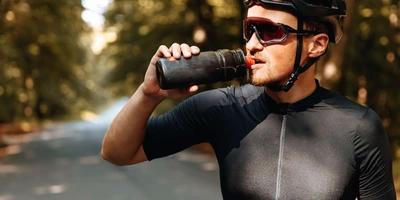 Radfahrer mit Sonnenbrille trinkt aus Trinkflasche