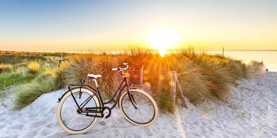Fahrrad steht am Strand in den Dünen im Sonnenuntergang