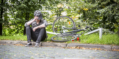Radfahrer sitzt am Wegrand nach einem Sturz mit kaputtem Fahrrad