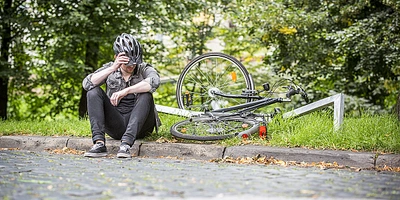 Radfahrer sitzt am Wegrand nach einem Sturz mit kaputtem Fahrrad