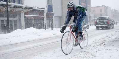 Radfahrer kämpft bei starkem Schneefall auf einer verschneiten Straße.