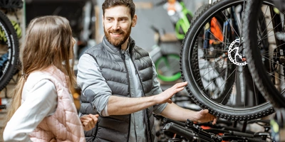 Worauf achten beim E-Bike Kauf? Fahrradverkäufer berät eine junge Frau in einem Fahrradladen