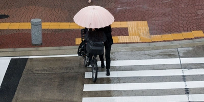 Person schiebt Fahrrad bei Regen über einen Zebrastreifen