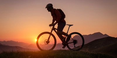 Mann fährt mit einem Mountainbike durch Gebirge im Sonnenuntergang