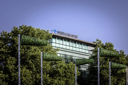 Moderne Bürogebäude umgeben von Bäumen und bunten Windfahnen im Vordergrund.