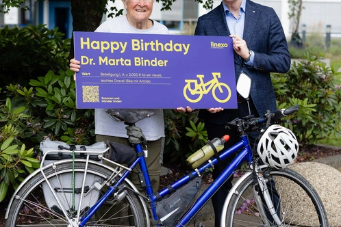 Zwei Personen stehen neben einem Fahrrad und halten ein Schild zum Geburtstag.