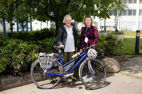 Zwei Personen stehen lächelnd neben einem blauen Fahrrad im Freien.