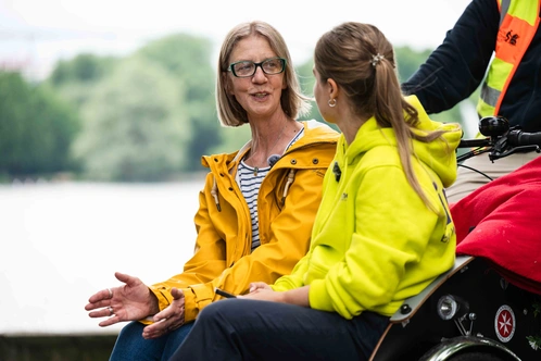 Zwei Frauen im Gespräch, eine in gelber Jacke, die andere in neon-grüner Kleidung.