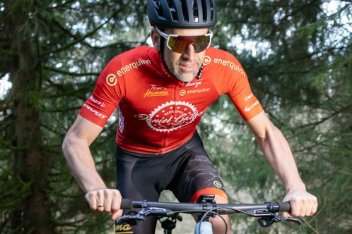 Ein Radfahrer in einem roten Trikot fährt durch einen Wald.